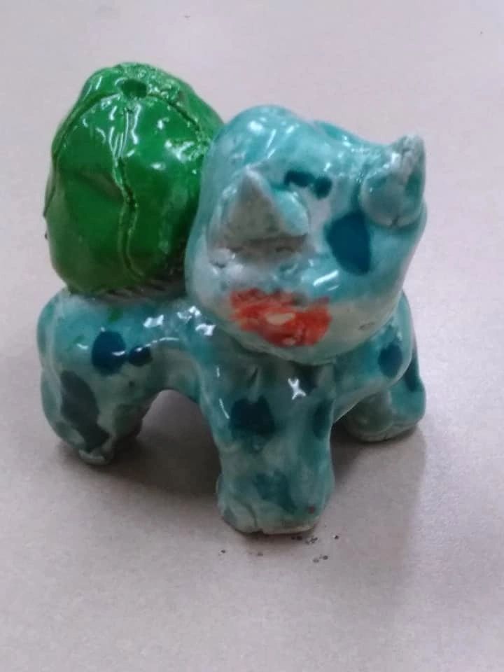 A small clay figure of a spotted turquoise creature with a green shell-like bump on its back, glazed and glossy.