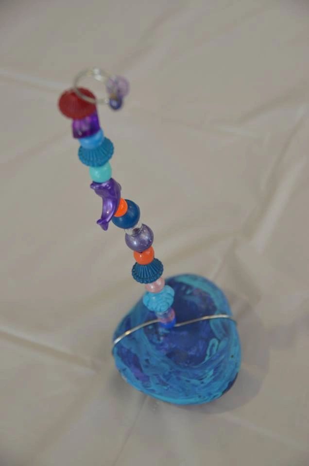 A stone painted white with a blue paint-dabbed flower pattern, resting beside a cup of blue paint and a sponge dauber.