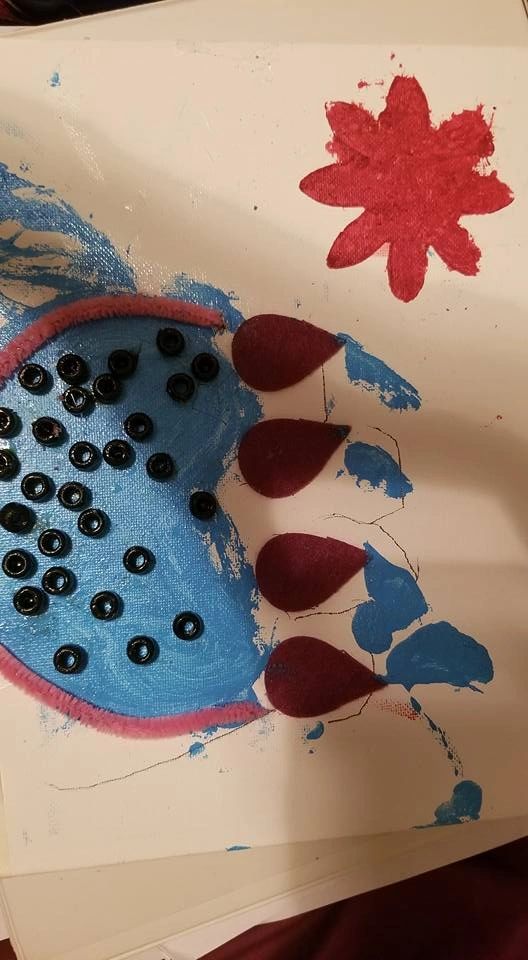 A canvas with a blue textured circle bordered in pink, dotted with black gem buttons, paired with a red glitter flower shape in the corner.