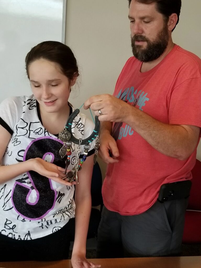 A volunteer helps an artist hold up a horseshoe decorated with silver charms, keys and coloured beads.