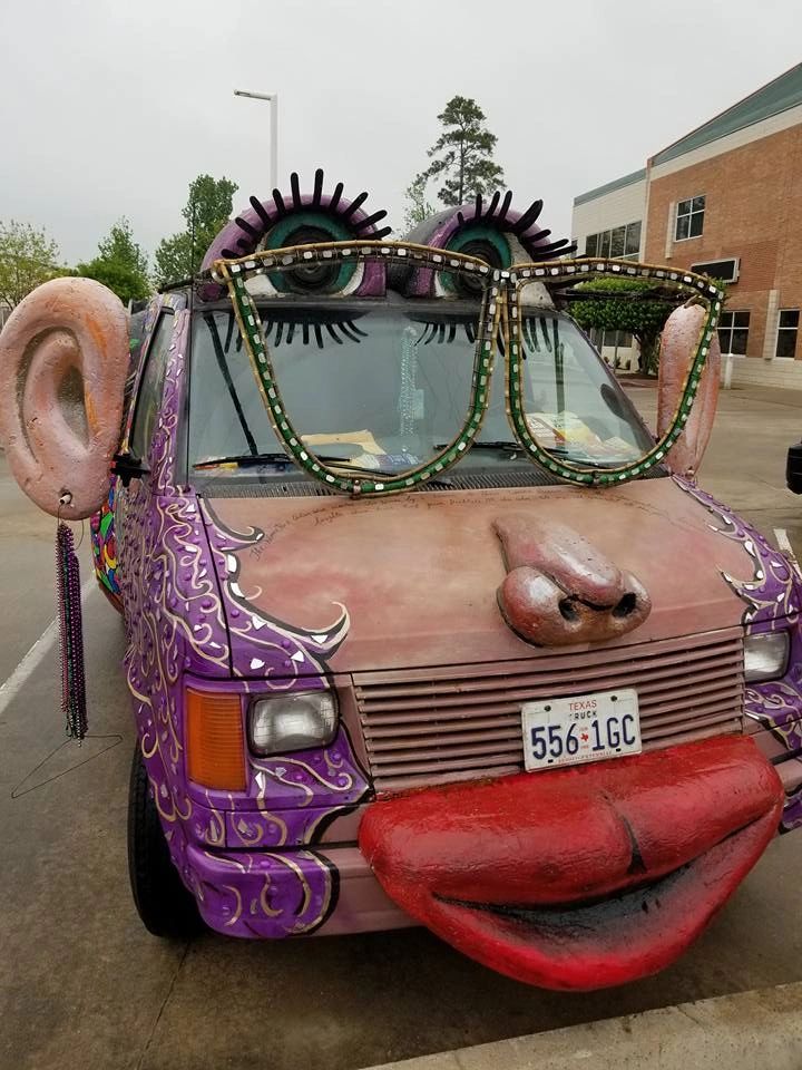 The front of the Women Rock Art Car, painted with a large nose, red lips and framed by lash-lined eyes above the windshield, with a sculpted ear and beaded fringe on one side.