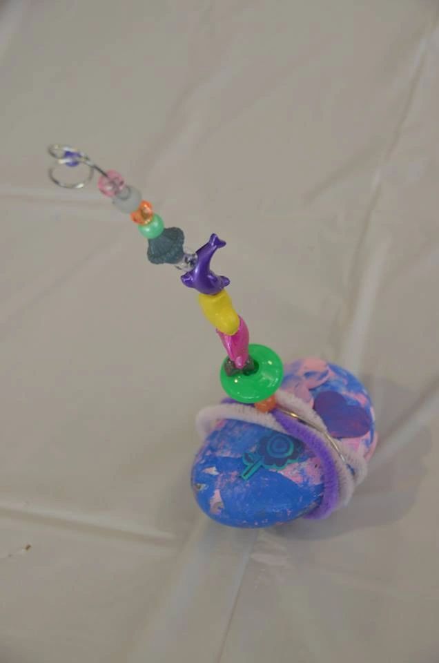 A beaded wand rising from a painted stone base decorated with a small flower sticker, the beads in shades of blue, pink, orange and yellow leading up to a purple charm.