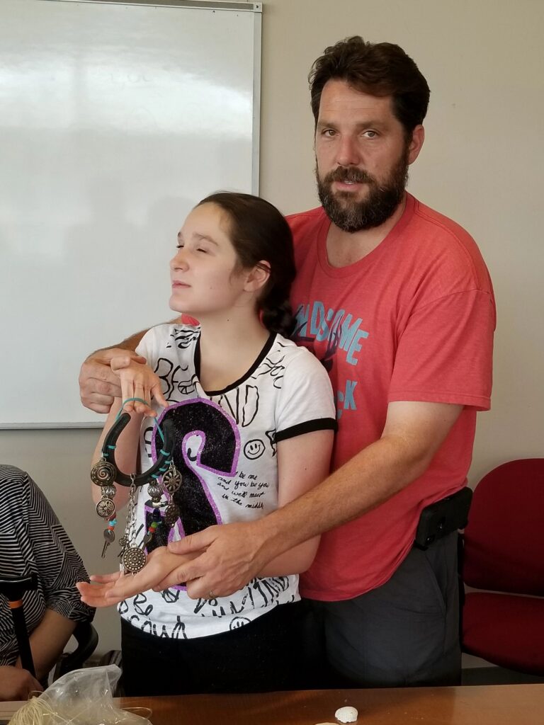 A volunteer stands beside an artist, both holding a horseshoe decorated with silver charms and beads.