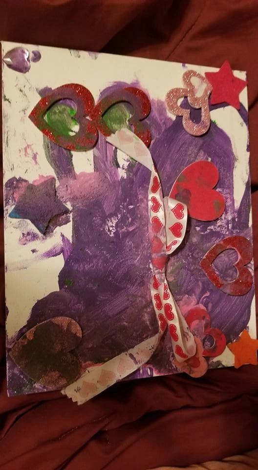 A canvas with a textured blue circle dotted with black glass gems, bordered by a pink pipe cleaner, paired with a red glitter flower and painted maroon petal shapes.