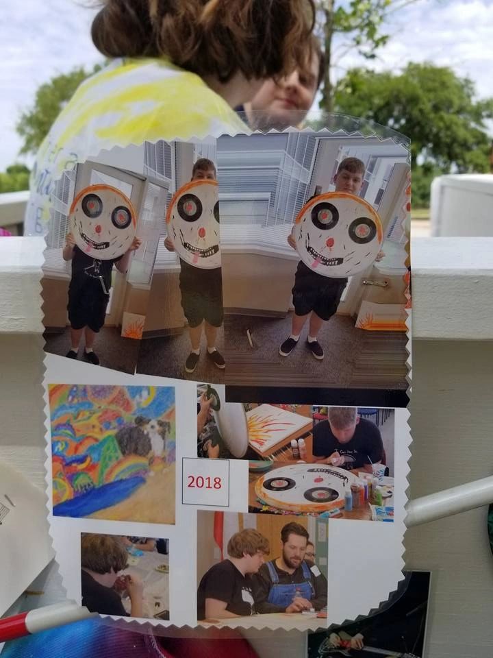 A laminated collage of photographs showing artists holding painted plate faces with painted expressions, a crayon drawing, and artists working on decorated records, labelled 2018.