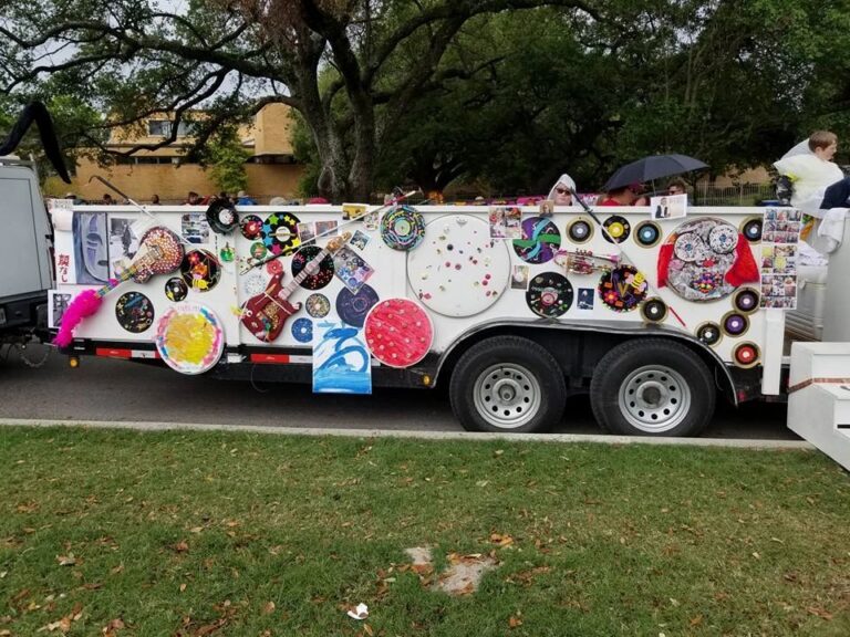 The side of the Creating With Blind Abandon parade float, covered edge to edge with decorated vinyl records, a jewelled guitar and painted canvases, parked under trees before the Houston Art Car Parade.