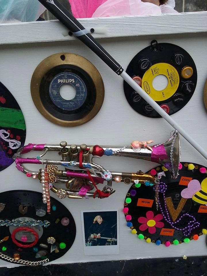 A close-up of decorated records on the float's panel: one framed in gold holding a Philips 45, another covered in bottle caps, and a silver trumpet decorated with ribbon and small charms.