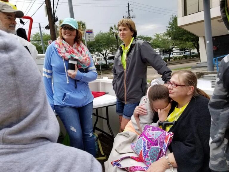 A small group stands together near the float, one person resting against another who wears a bright yellow raincoat.