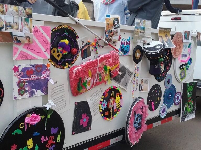 A close-up section of the float's decorated panel, covered in painted records, a beaded name plate, tissue-paper art and a small hand drum.