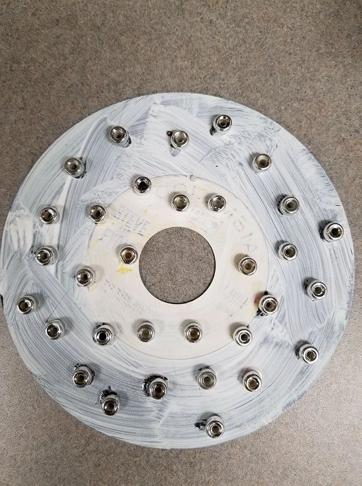 A white-painted record studded edge to edge with silver nuts arranged in concentric rings.