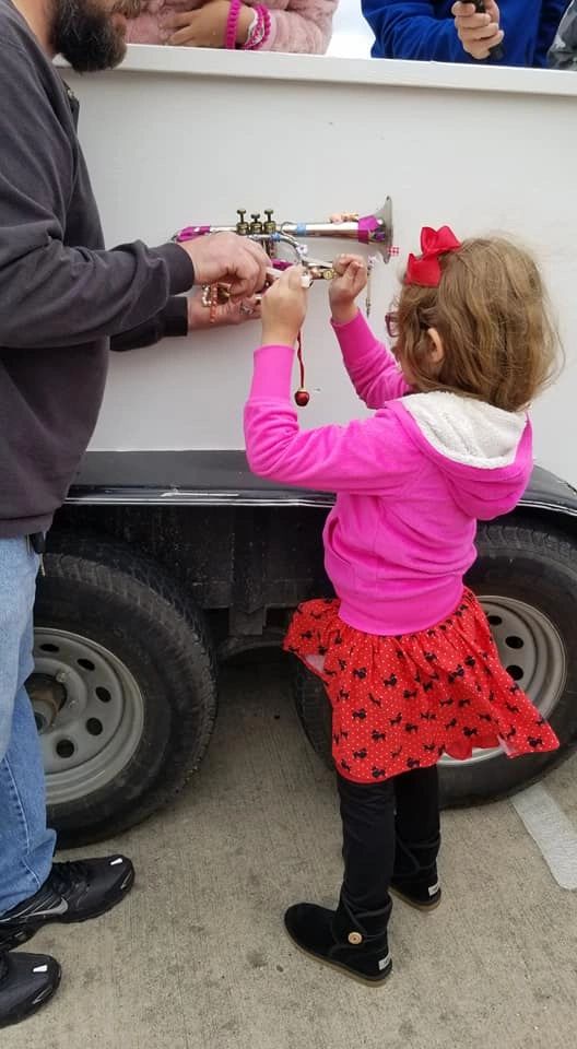 A volunteer helps a young artist attach small charms to a decorated trumpet mounted on the float's panel.