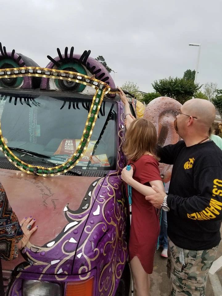 A volunteer guides an artist's hand across the sculpted ear on the Women Rock Art Car, with lash-lined eyes and gold trim on the windshield above.