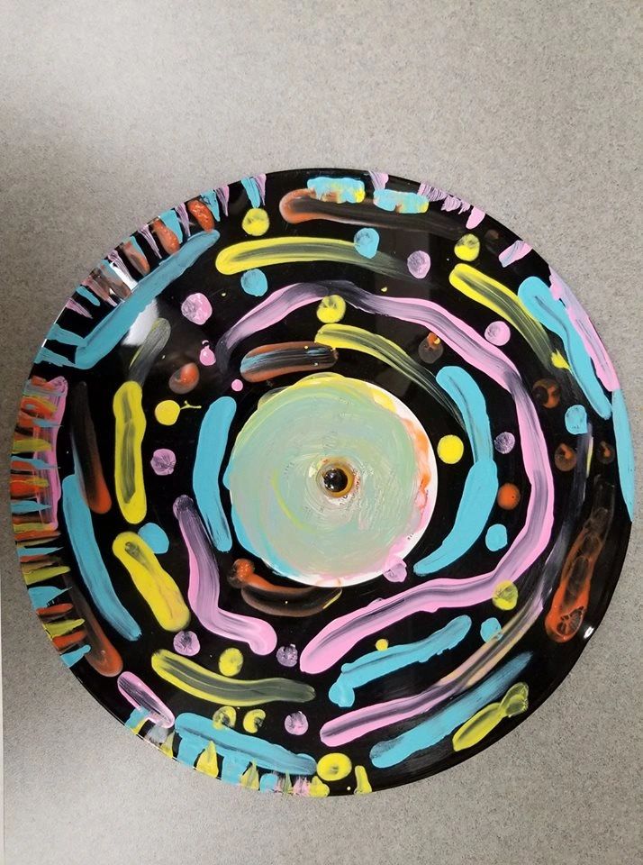 A black record painted with concentric rings of pink, blue and yellow brushstrokes radiating from the centre hole.