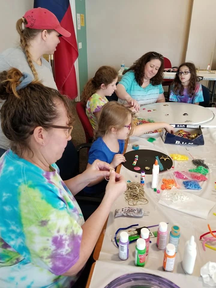 Artists and volunteers sit around a table covered in beads, pipe cleaners and paint, working on a decorated record.