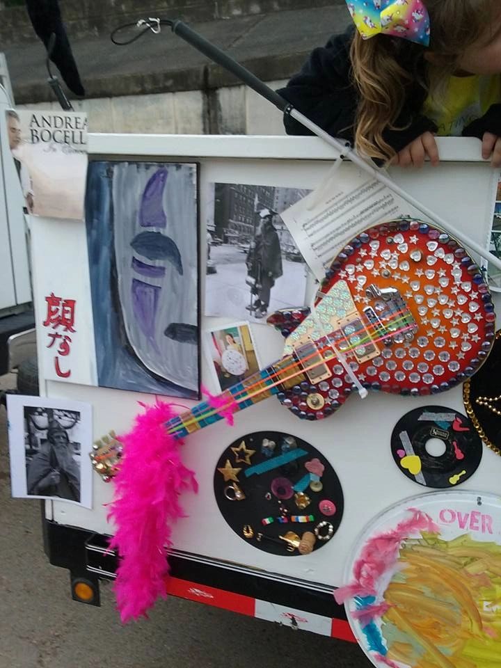 A close-up of the float's panel showing a painted canvas, a jewelled electric guitar with a pink feather boa strap, and small framed photographs.