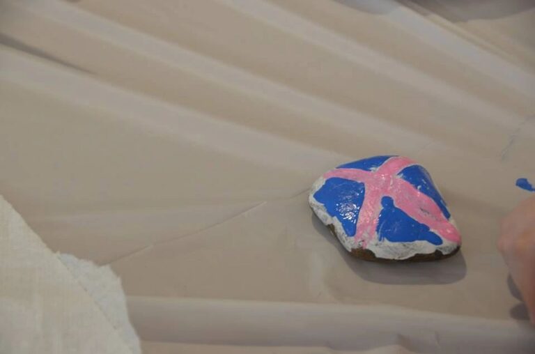 A stone painted blue with a pink starfish shape brushed on top, resting on a table.