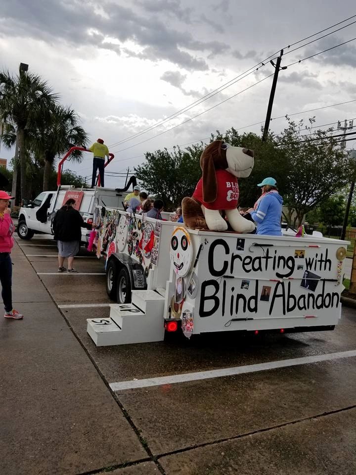 The back of the float in a parking area, with the stuffed hound mascot on top and Creating With Blind Abandon painted across the panel in large letters.