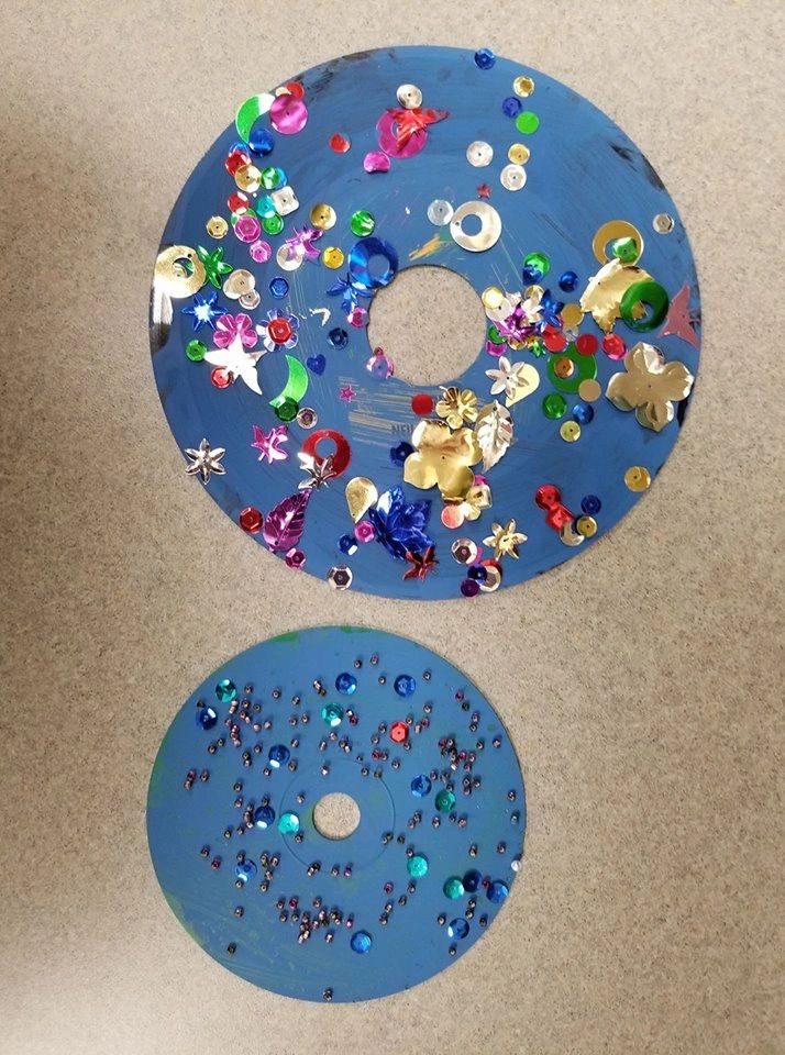 Two decorated records side by side: a large one covered in sequins, gems and metallic flower shapes, a smaller one dotted with blue sequins and beads.