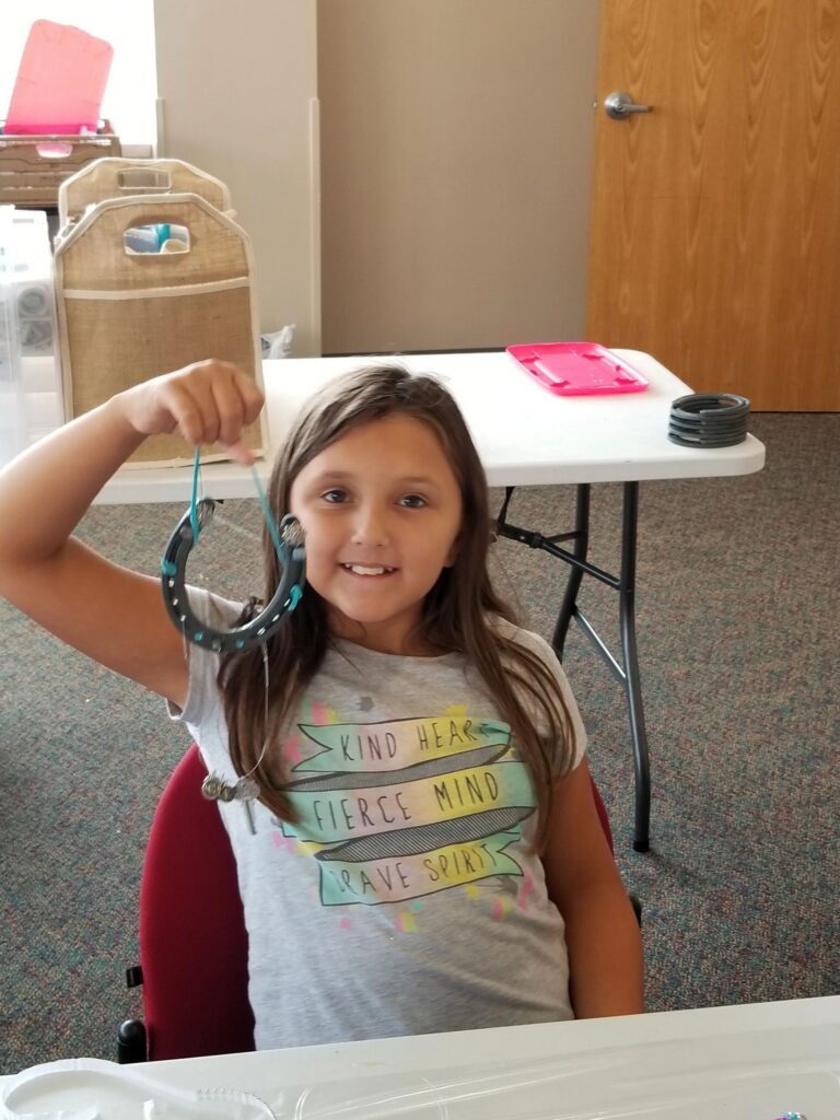 An artist holds up a horseshoe wrapped in teal cord, decorated with a small key charm hanging beneath it.