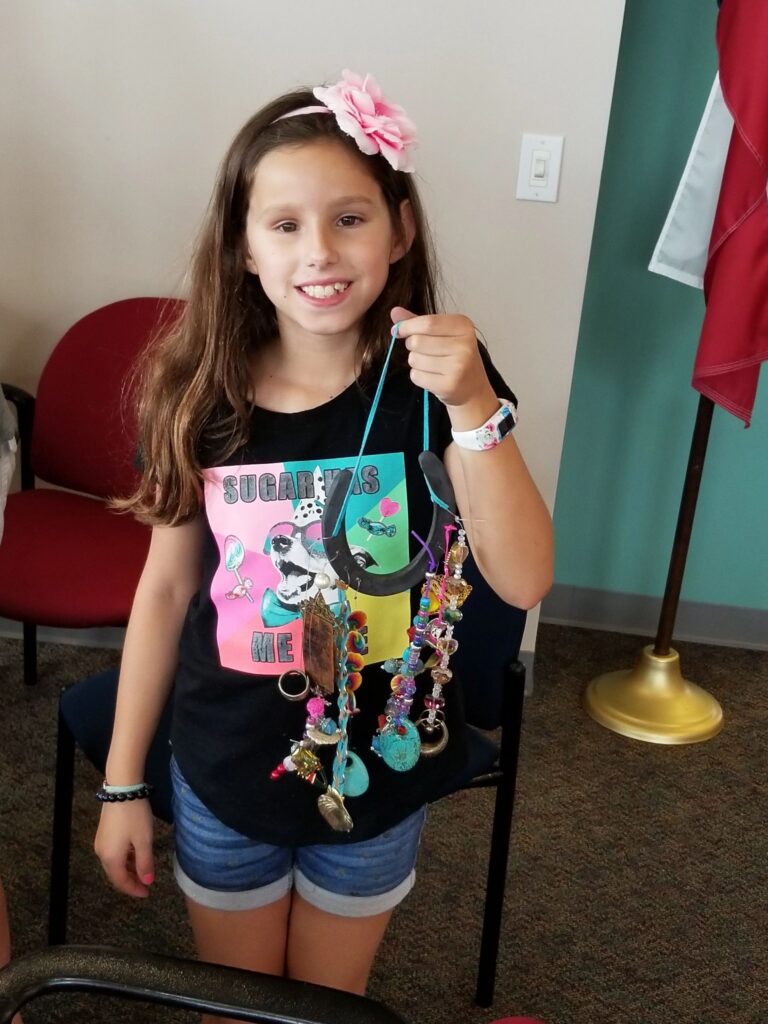 An artist holds up a finished horseshoe necklace hung with beaded strands, charms and a turquoise stone.