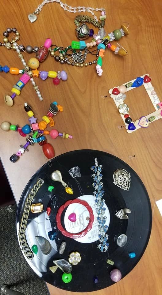 A collection of beaded ornaments on a table: two star-shaped bead figures, a small popsicle-stick picture frame, and a black record decorated with charms, pendants and small trinkets.