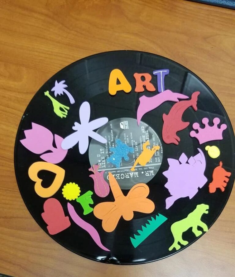 A black vinyl record decorated with a ring of foam craft shapes including animals, flowers and a heart, spelling the word ART in coloured foam letters at the top.