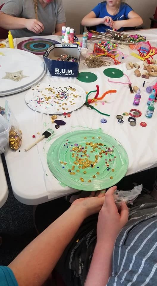 A record painted mint green and dotted with gold sequins, resting on a table covered in pipe cleaners, bottle caps and craft supplies.