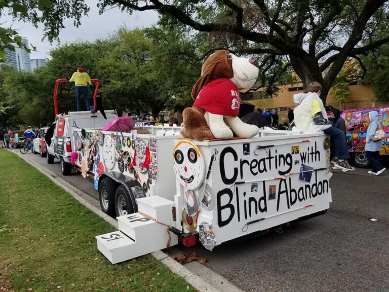 The back of the parade float with a giant stuffed hound wearing a Blind to the Bone shirt, and Creating With Blind Abandon painted in large letters across the panel.