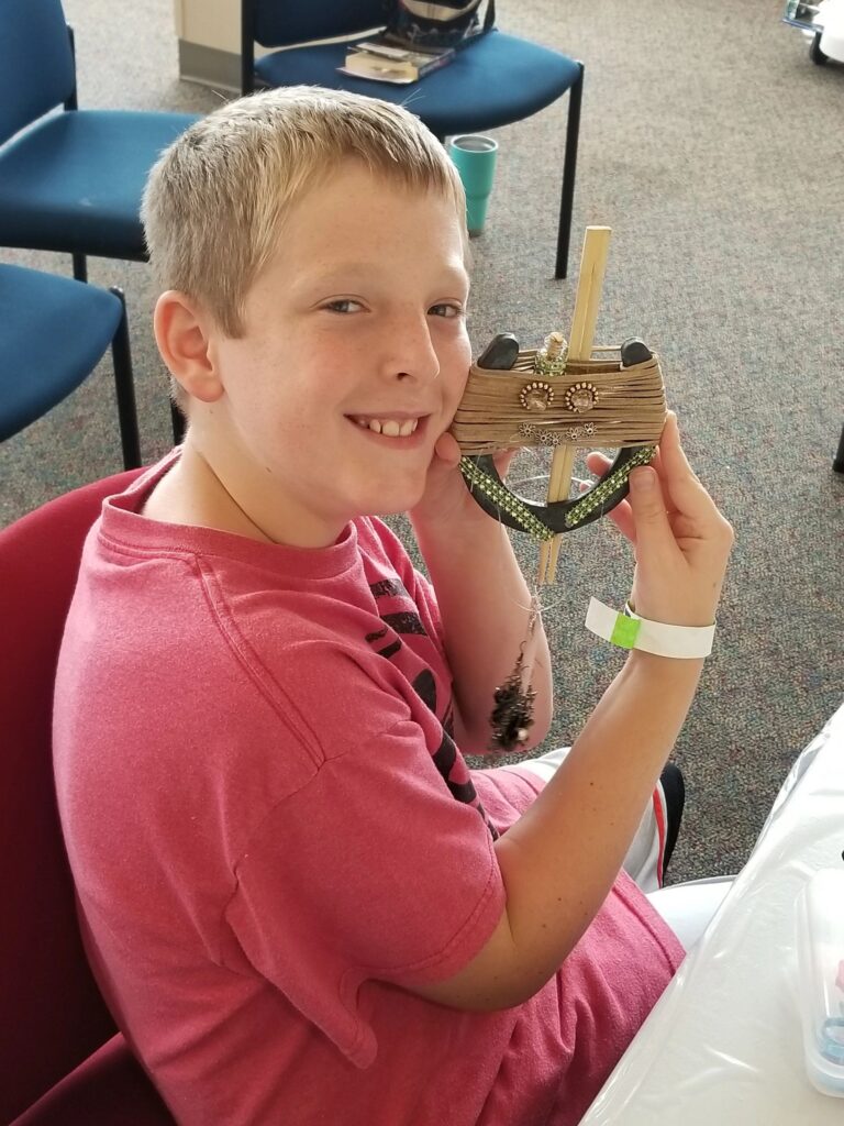 An artist holds up a finished horseshoe decorated with twine wrapping, small gems and a wooden dowel accent.