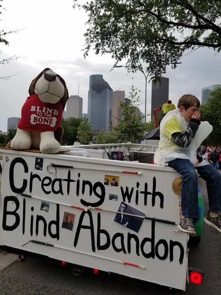 The float travels down the parade route with the Houston skyline in the background, the raised platform rider visible ahead on the towing truck.