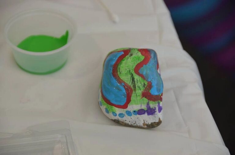 A painted stone with a red, green and blue swirl pattern and a beaded strand strung with red, white and green stripes ending in a blue clip charm.