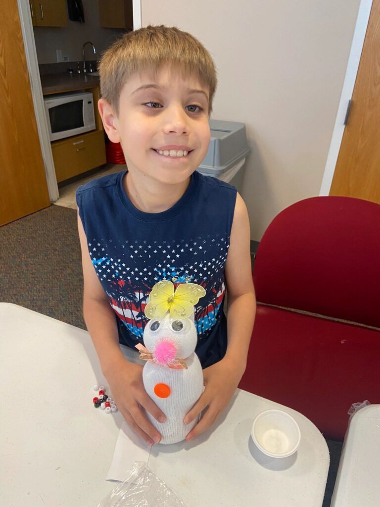 An artist smiles while holding a finished sock bunny with googly eyes, a pink pom-pom nose and an orange button on its body.