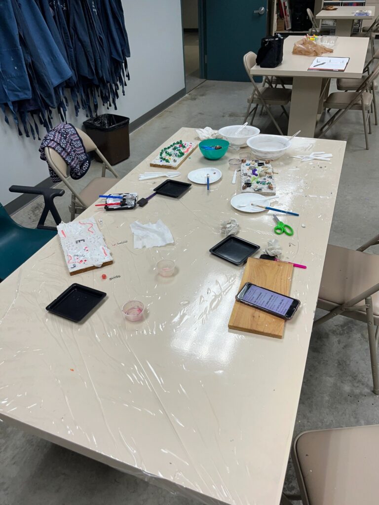 A wide view of a worktable covered in newspaper and paint trays, with a jigsaw-puzzle heart taking shape from pink and red painted pieces.