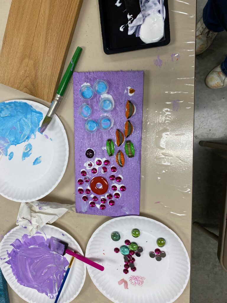 A finished purple board decorated with rows of glass gems in blue, green and pink, plus glass shell shapes, arranged in patterned columns.
