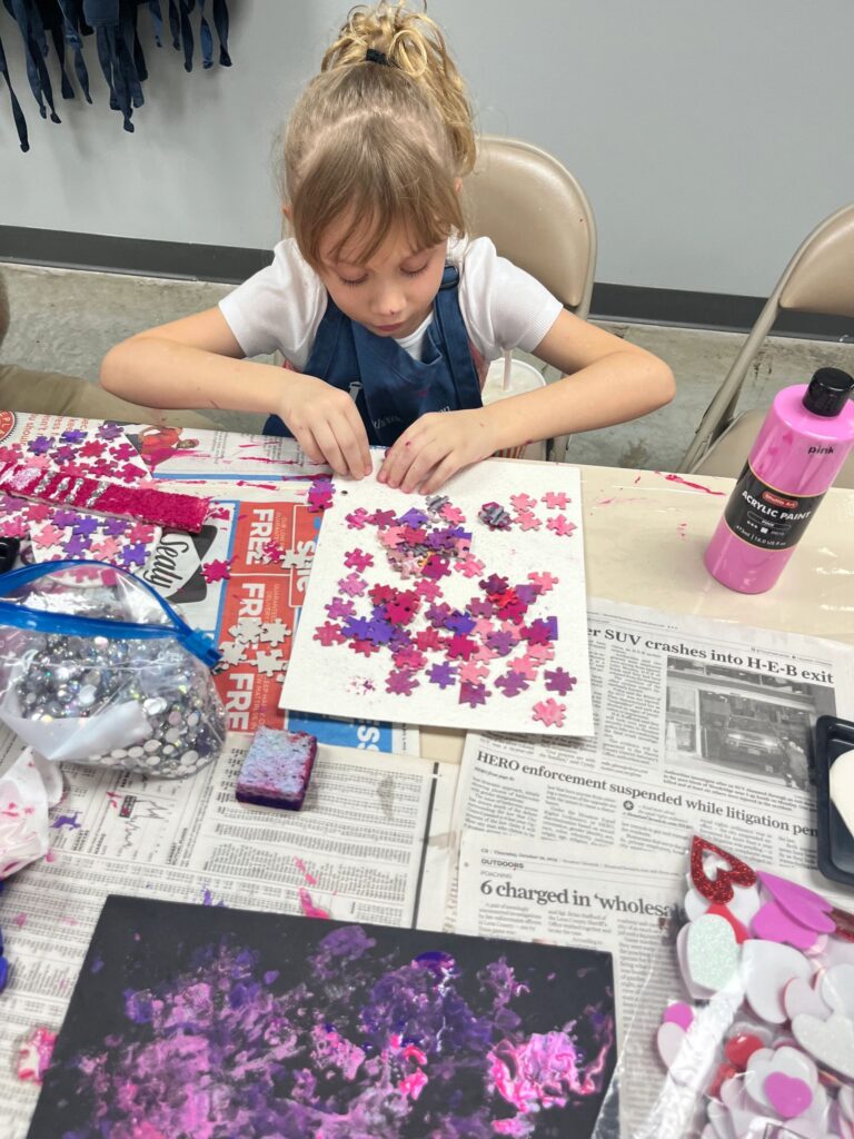 An artist holds up a heart made from red and pink jigsaw-puzzle pieces, with a beaded braille bar spelling LOVE across the centre.